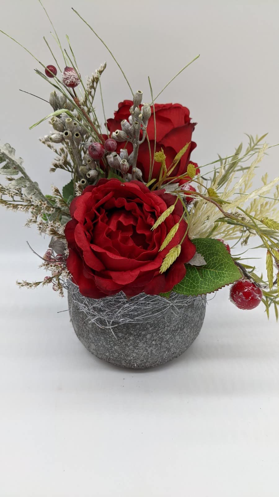 Rotes Rosengesteck im grauen Steintopf mit Ähren, Rispen und grünem Blatt, von vorn fotografiert