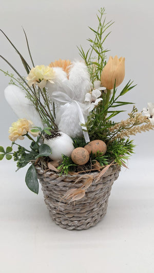Ostergesteck im Korb mit weißem Plüschhase, apricotfarbener Tulpe, cremefarbenen Ranunkeln und Eiern