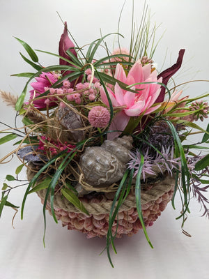 Sommergesteck von oben: rosa Seerose, pinke Blüten, Gräser und große Muschel in muschelbesetzter Schale