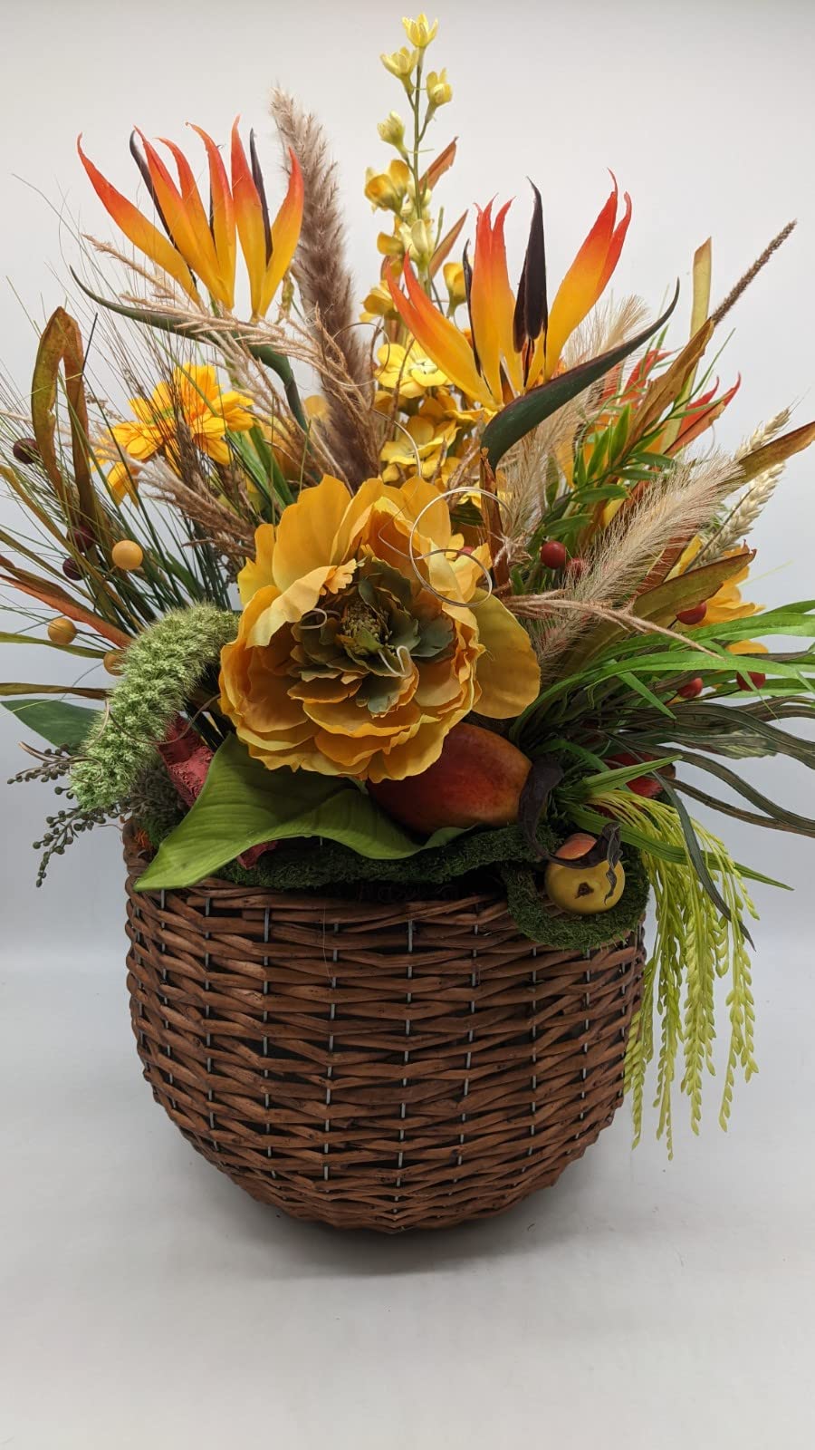 Hohes Herbstgesteck im braunen Weidenkorb mit orangeroten Strelizien, gelber Blüte, Mango und hellen Gräsern