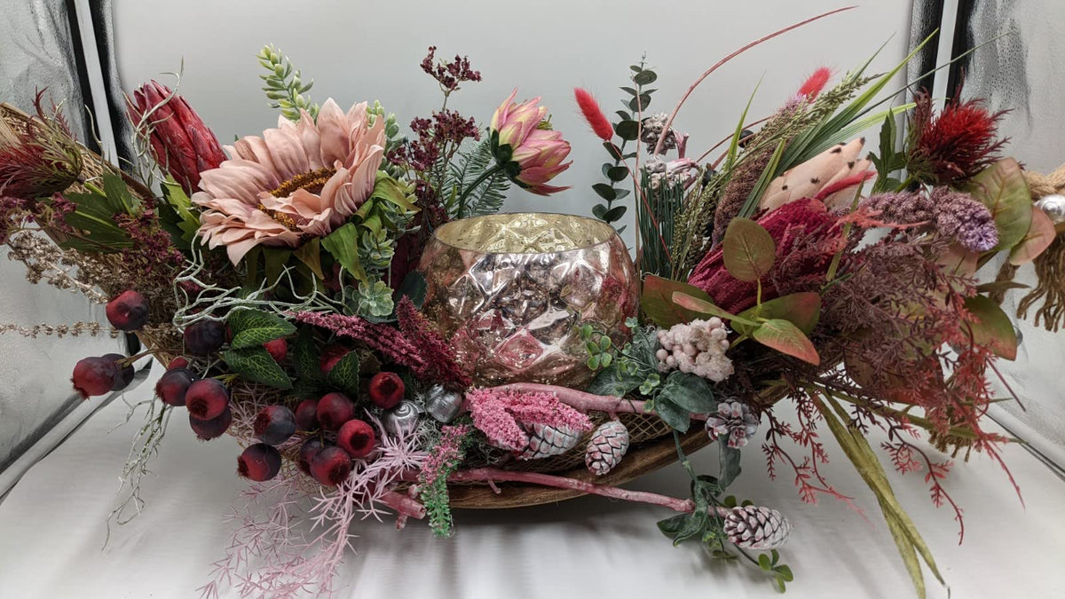 Langes Herbstgesteck in Holzschale mit rosé schimmerndem Windlicht, altrosa Sonnenblume, roten Beeren und Zapfen