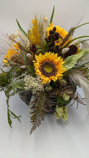 Sonnenblumengesteck von vorn: gelbe Blüten, grüne Hopfendolden, braunes Farnlaub und Banksia im Korb