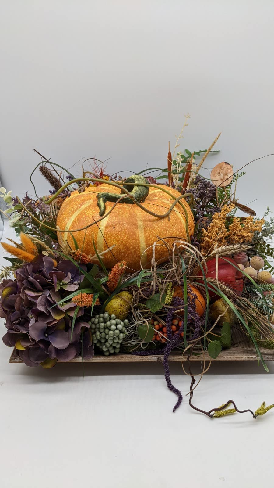 Herbstgesteck im Holztablett mit orangefarbenem Kürbis, lila Hortensie, Beeren, Ähren und Gräsern