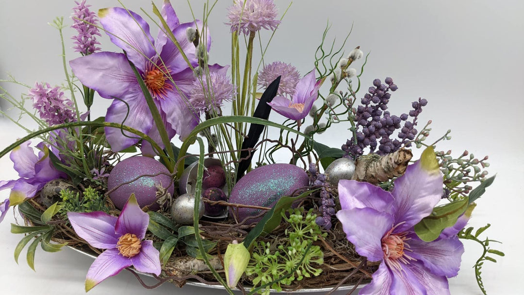 Ostergesteck Frühlingsgesteck Tischgesteck Clematis Wiesenblumen Eier Feder Gräser lila silber