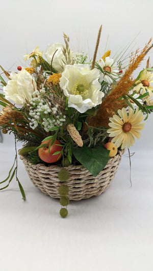 Herbstgesteck im Naturkorb mit cremeweißen Mohnblüten, Margeriten, Gräsern, rotem Apfel und grünen Blättern