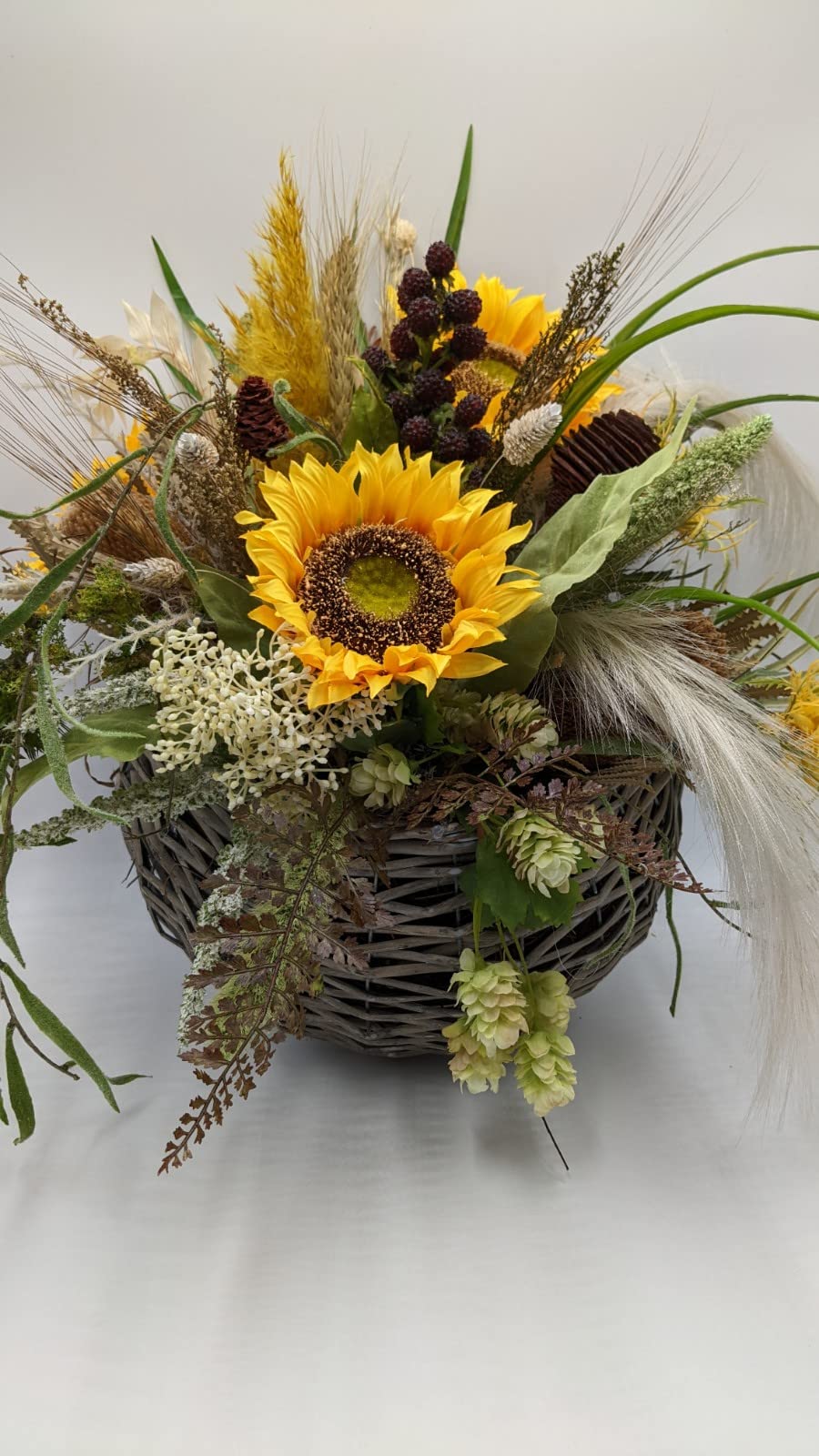 Herbstgesteck im grauen Weidenkorb mit gelben Sonnenblumen, dunklen Beeren, Ähren und hellen Gräsern
