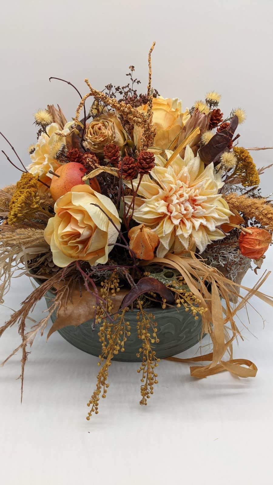 Herbstgesteck von vorn: Chrysantheme, Rose, orangefarbene Lampionblüten, gelbe Dolden und Bastbänder über dem Schalenrand