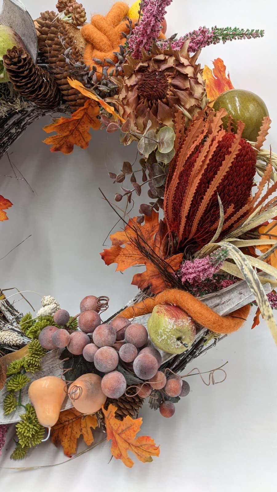 Ausschnitt des Herbstkranzes mit Banksia, Distelblüte, violetter Traube, Birne und Zapfen