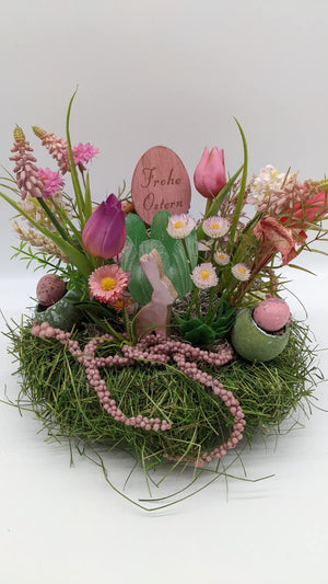Ostergesteck von vorn: Holzschild „Frohe Ostern", violette und rosa Tulpen, Gerbera und rosa Perlenkette