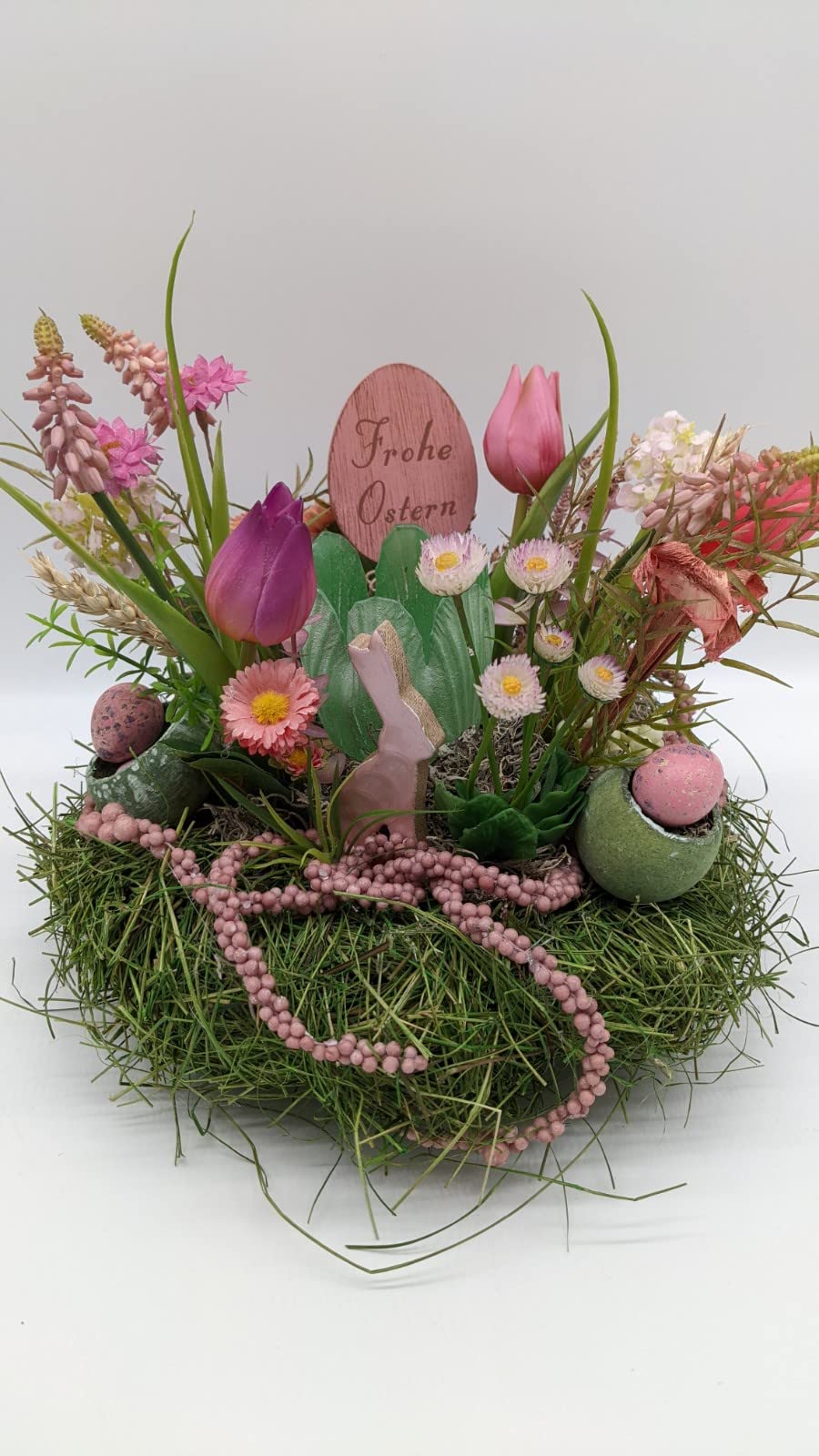 Ostergesteck von vorn: Holzschild „Frohe Ostern", violette und rosa Tulpen, Gerbera und rosa Perlenkette
