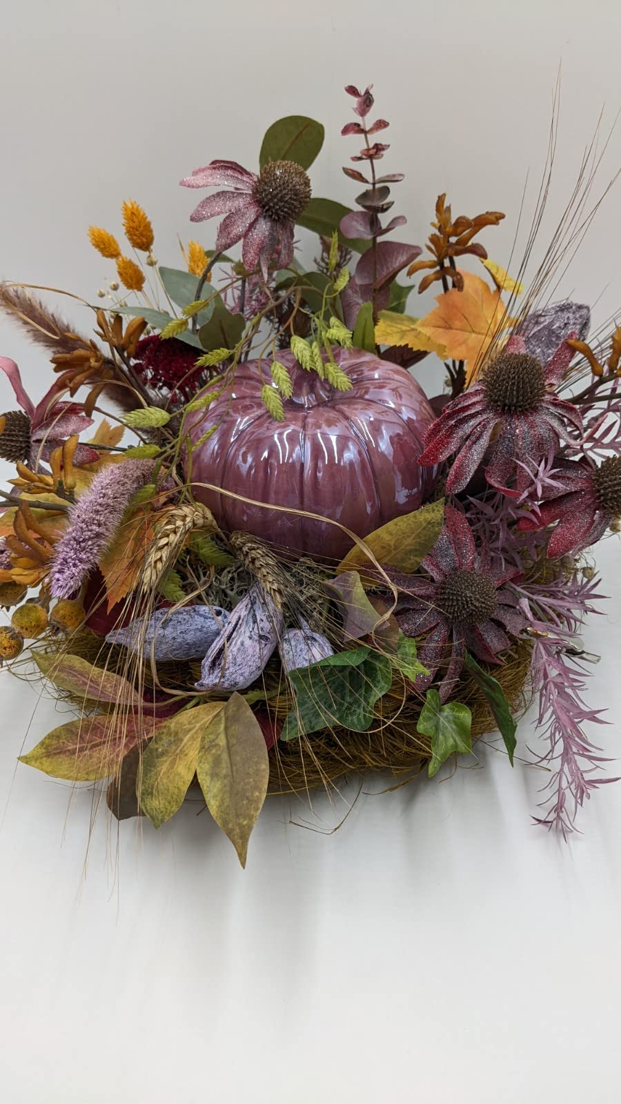 Herbstgesteck von vorn: glänzender Kürbis in Lila, umgeben von Ähren, Herbstblättern, Beeren und Efeu