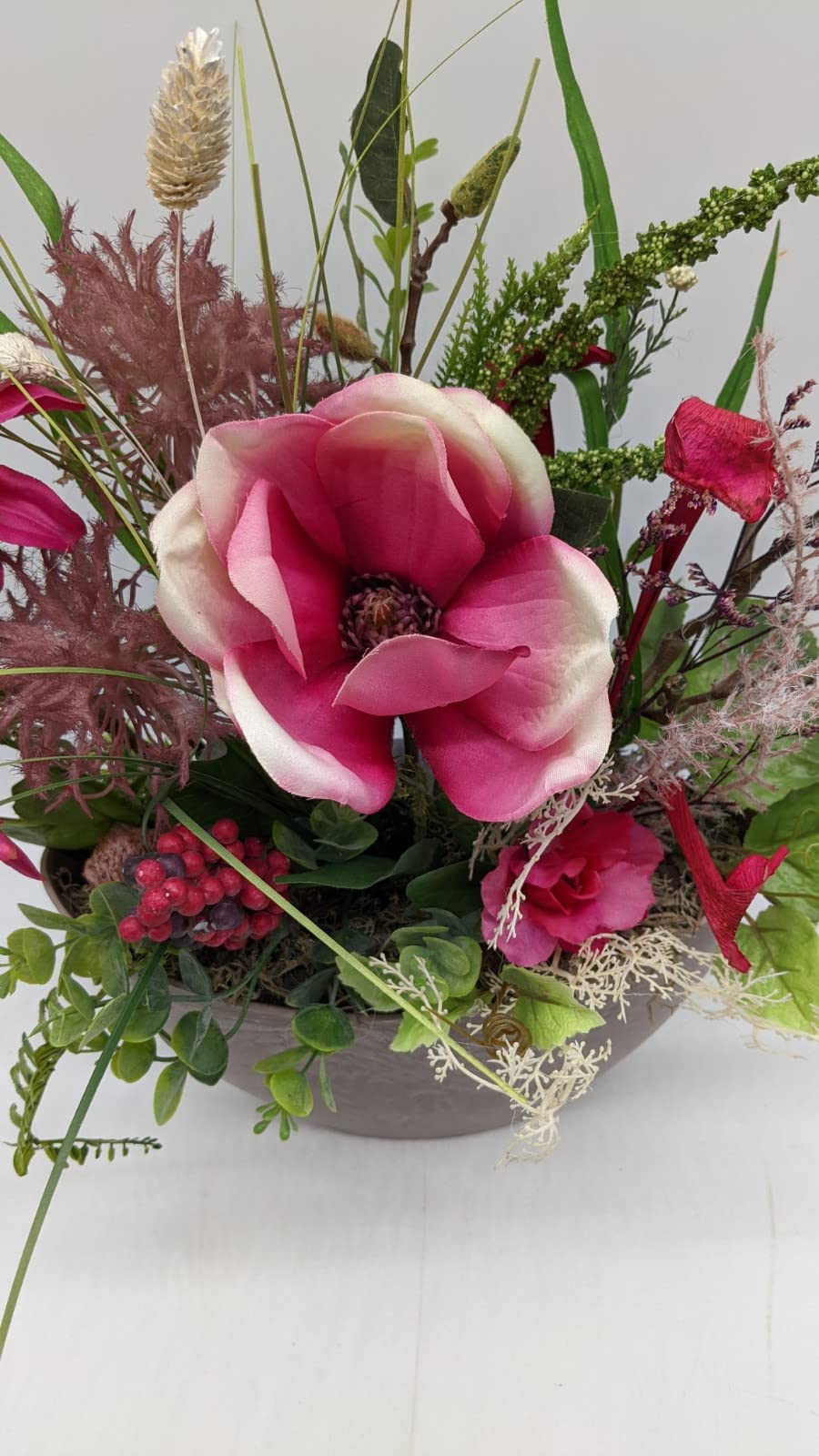 Nahaufnahme der pinken Magnolienblüte mit cremefarbenen Rändern, Beerendolde und Eukalyptus im Gesteck