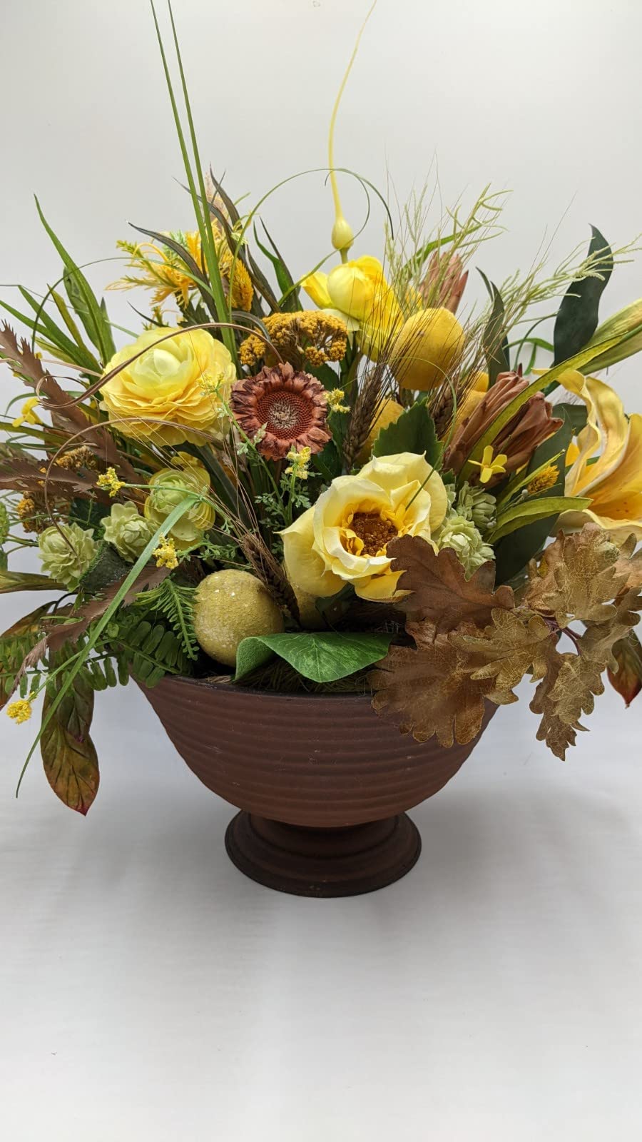 Herbstgesteck in brauner Pokalschale mit gelben Rosen, rostbrauner Sonnenblume, Zitronen und Gräsern