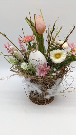 Frühlingsgesteck rosa weiß mit Tulpe, Knospenzweigen, Gräsern und beschriftetem Ei im Heunest