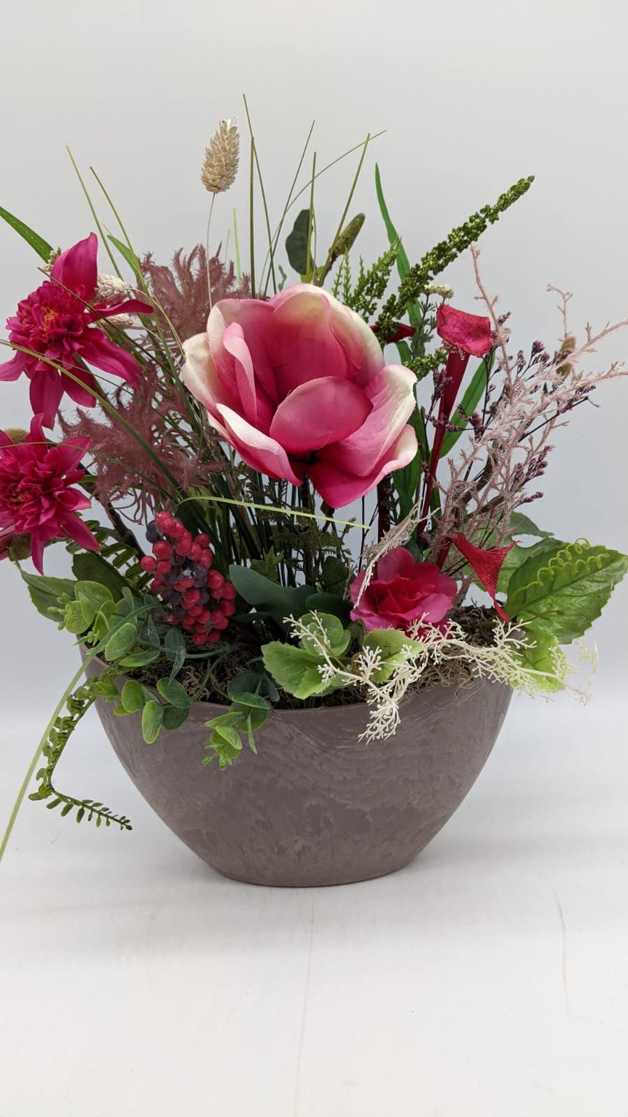 Tischgesteck in grauer Schale mit pinker Magnolie, Dahlien, roten Beeren und grünen Gräsern