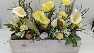 Frühlingsgesteck in weißem Holzkasten mit gelbem Mohn, weißen Callas, Tulpen, Schneckenhaus und Gräsern