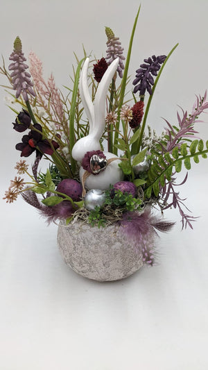 Frühlingsgesteck von vorn: Hase mit Silberherz, Farn, Gräser, Beeren-Eier und Federn in Lila und Weiß