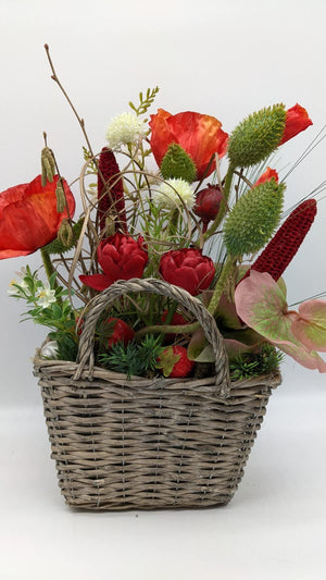 Frühlingsgesteck im grauen Henkelkorb mit rotem Mohn, roten Tulpen, weißen Blüten und grünen Fruchtständen