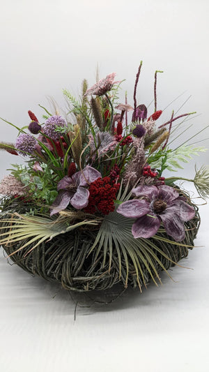 Herbstgesteck auf dunklem Zweigkranz mit lila Blüten, roten Beeren, Allium und Gräsern, seitlich fotografiert