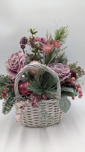 Wintergesteck im weißen Korb mit altrosa Rosen, Kugeln, Tanne und Zapfen, dazwischen feine LED-Lichterkette