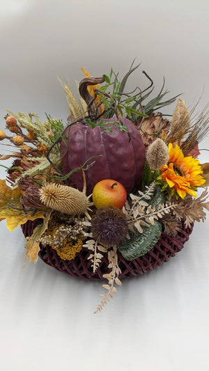 Herbstgesteck von vorn: Kürbis, Apfel, Sonnenblume, Karden, Weizenähren und gelbes Herbstlaub im Flechtkorb