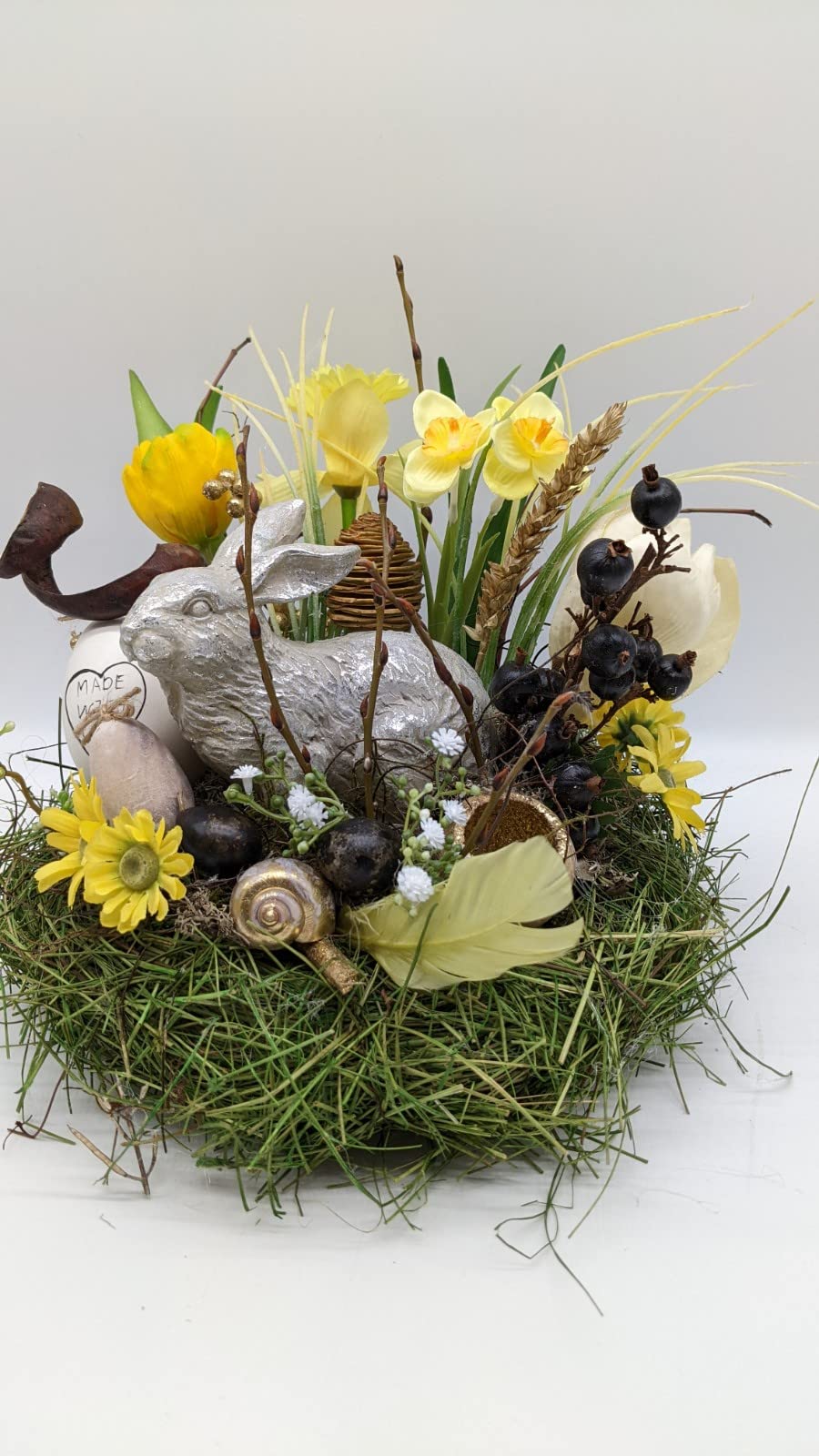 Ostergesteck im Grasnest mit silbernem Hasen, gelben Narzissen, Eiern und Feder, seitlich fotografiert