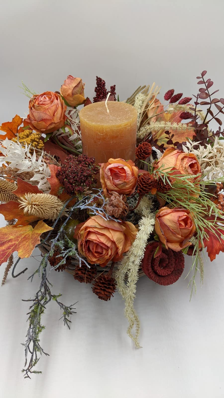 Herbstgesteck von oben: orange Rosen, rote Beeren, Herbstlaub und weiße Gräser rund um die Kerze
