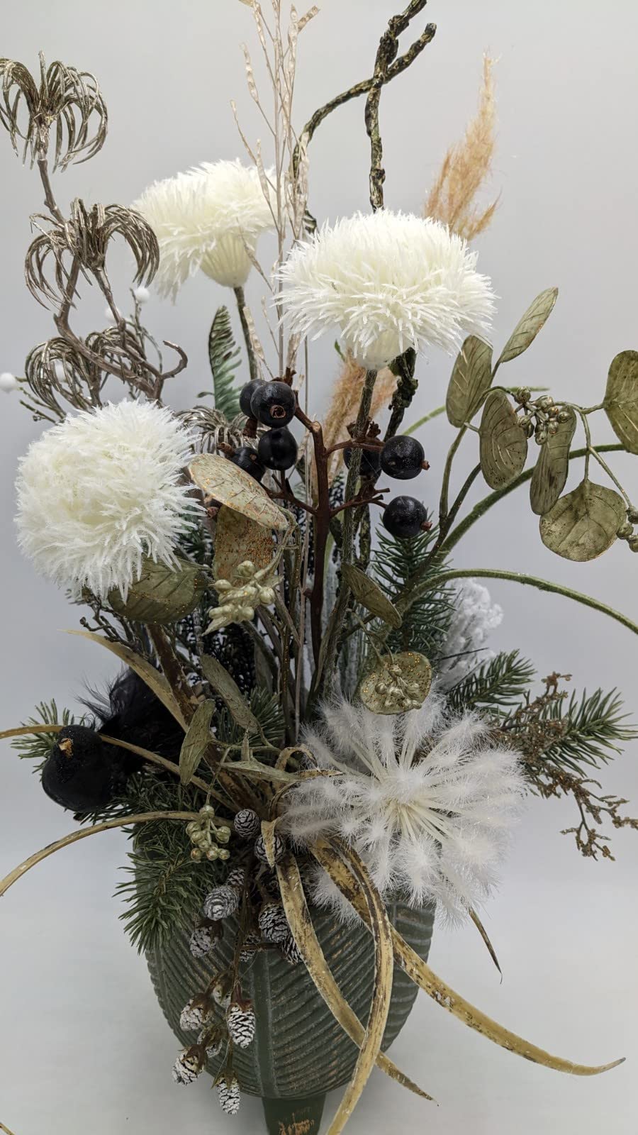 Nahaufnahme des Wintergestecks mit schwarzem Vogel, weißer Federblüte, goldgrünen Blättern und Gräsern