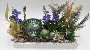 Frühlingsgesteck von vorn: Teelichtglas, violette Blüten, hellblaue Hyazinthen, Gräser, Moos und grüne Ostereier