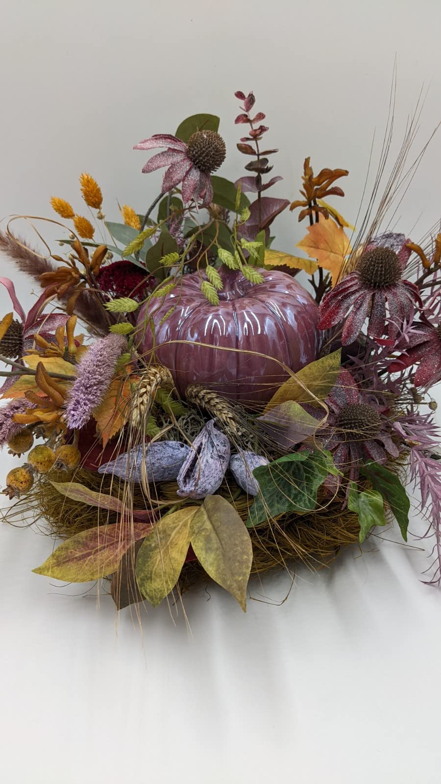 Herbstgesteck mit altrosa Kürbis, rosa Sonnenhut, Eukalyptus und Gräsern im Nest, seitlich fotografiert