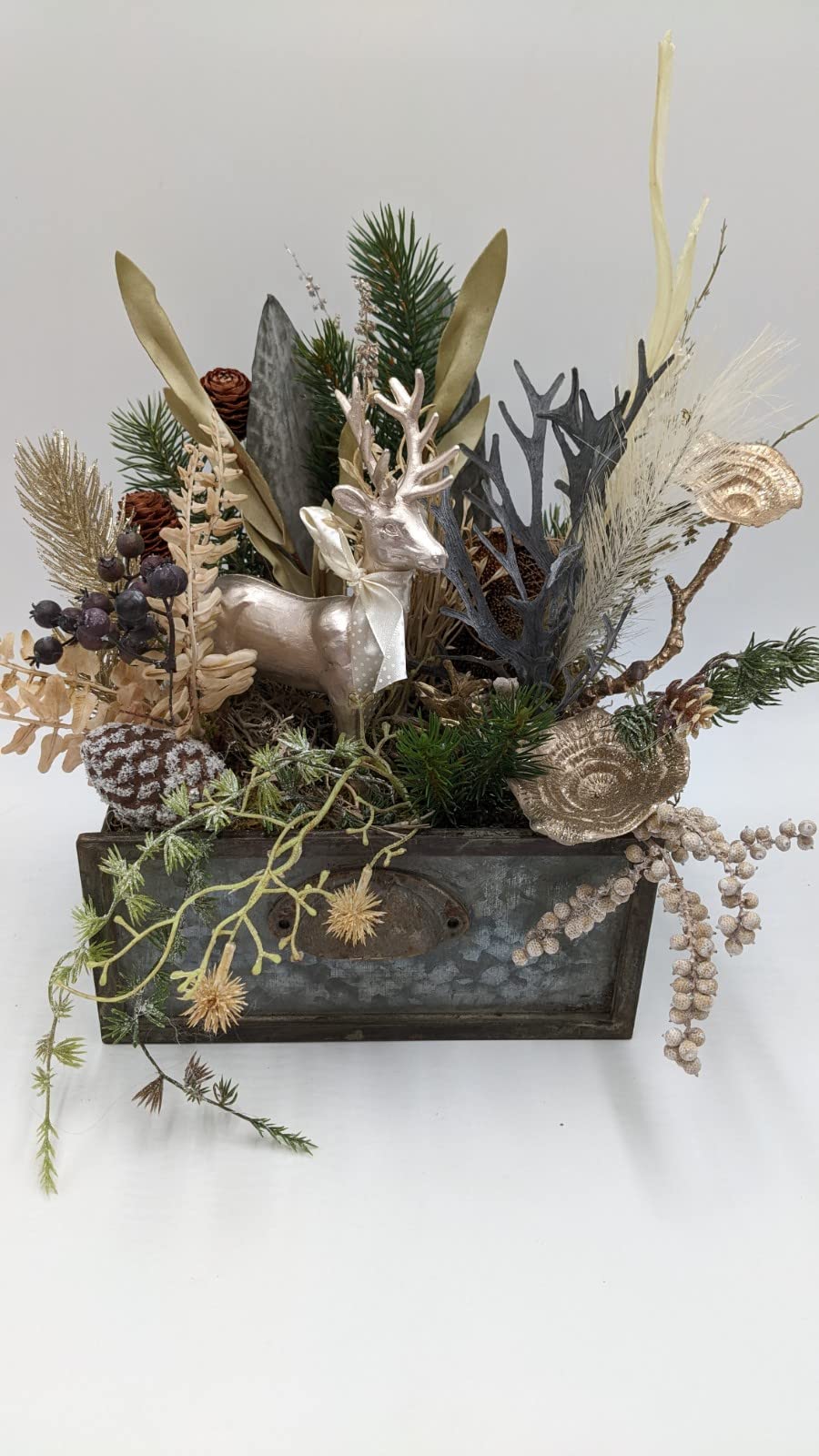 Weihnachtsgesteck creme gold mit Hirsch, Geweihzweigen, beschneitem Zapfen und hellen Gräsern in alter Zinkschublade