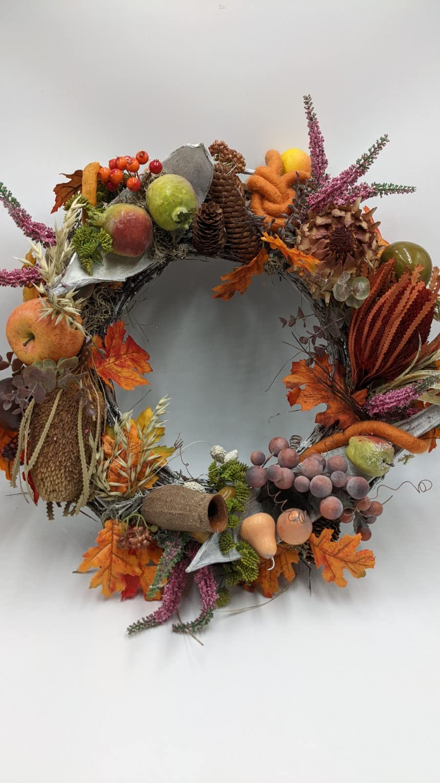 Runder Herbstkranz mit Äpfeln, Birnen, Zapfen, Banksia, rosa Heide und orangem Laub auf hellem Reisigring