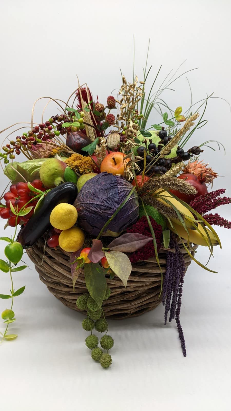 Herbstgesteck im Weidenkorb mit Rotkohl, Aubergine, Äpfeln, Zitronen, Beeren und Gräsern, seitlich fotografiert