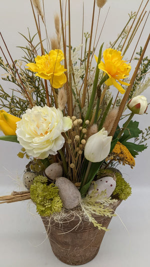 Nahaufnahme des Ostergestecks mit weißer Tulpe, gelber Schafgarbe, Moos und gepunktetem Osterei