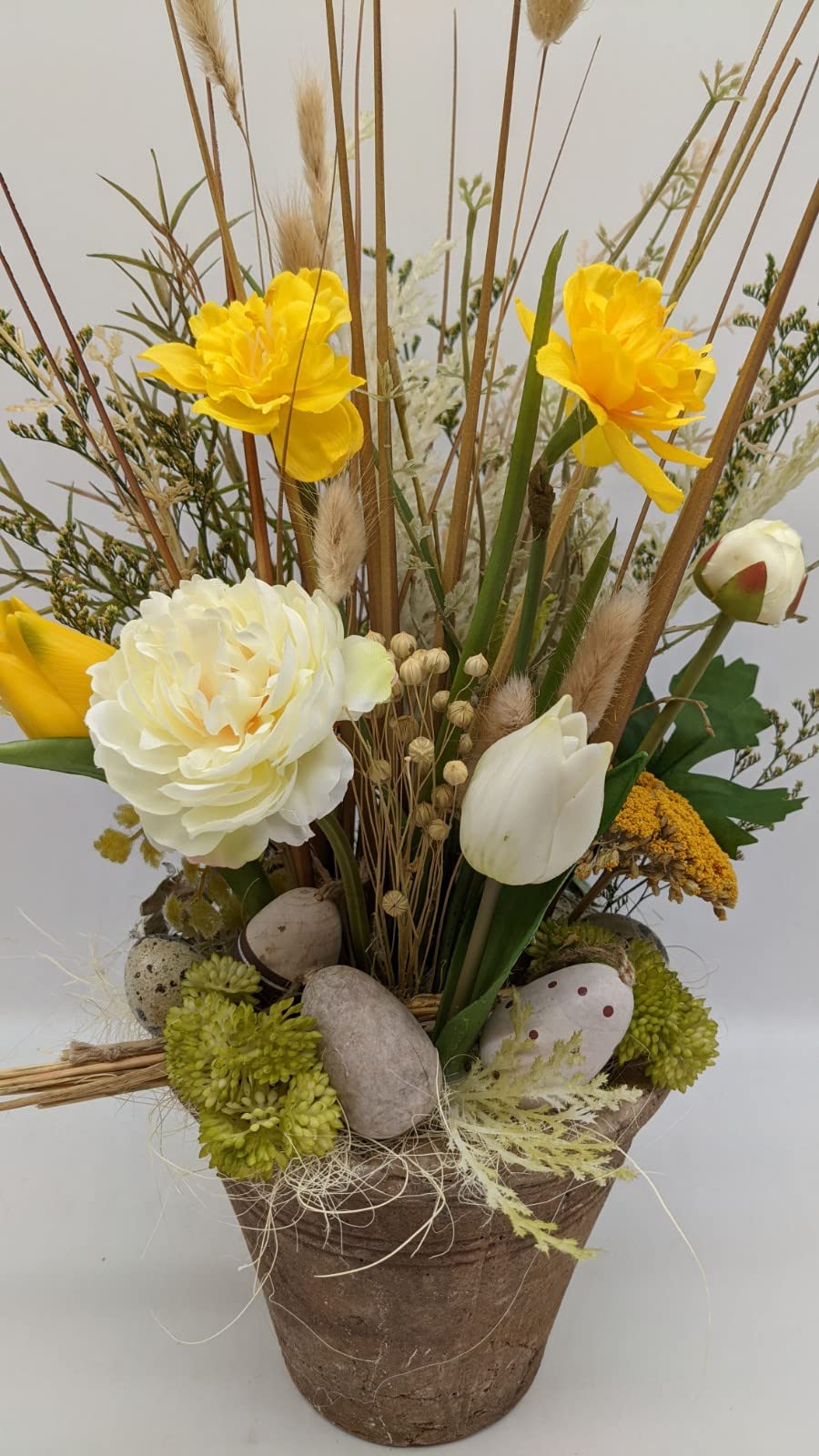 Nahaufnahme des Ostergestecks mit weißer Tulpe, gelber Schafgarbe, Moos und gepunktetem Osterei