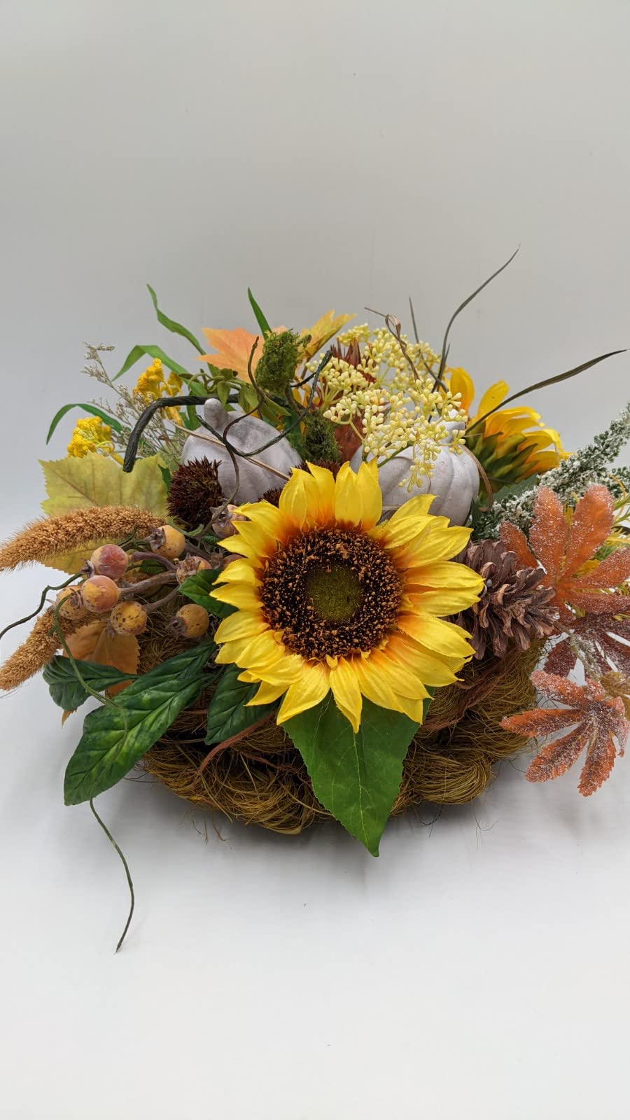 Herbstgesteck mit großer gelber Sonnenblume, zwei grauen Kürbissen, Hagebutten und Zapfen im Naturfasernest