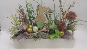 Ostergesteck im weißen Holzkasten mit Holzhäsin, goldenen Eiern, lila Allium und Gräsern