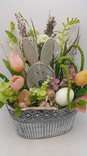 Ostergesteck von vorn: Holzhase zwischen rosa und orangen Tulpen, grünen Blättern, Moos und gesprenkelten Eiern