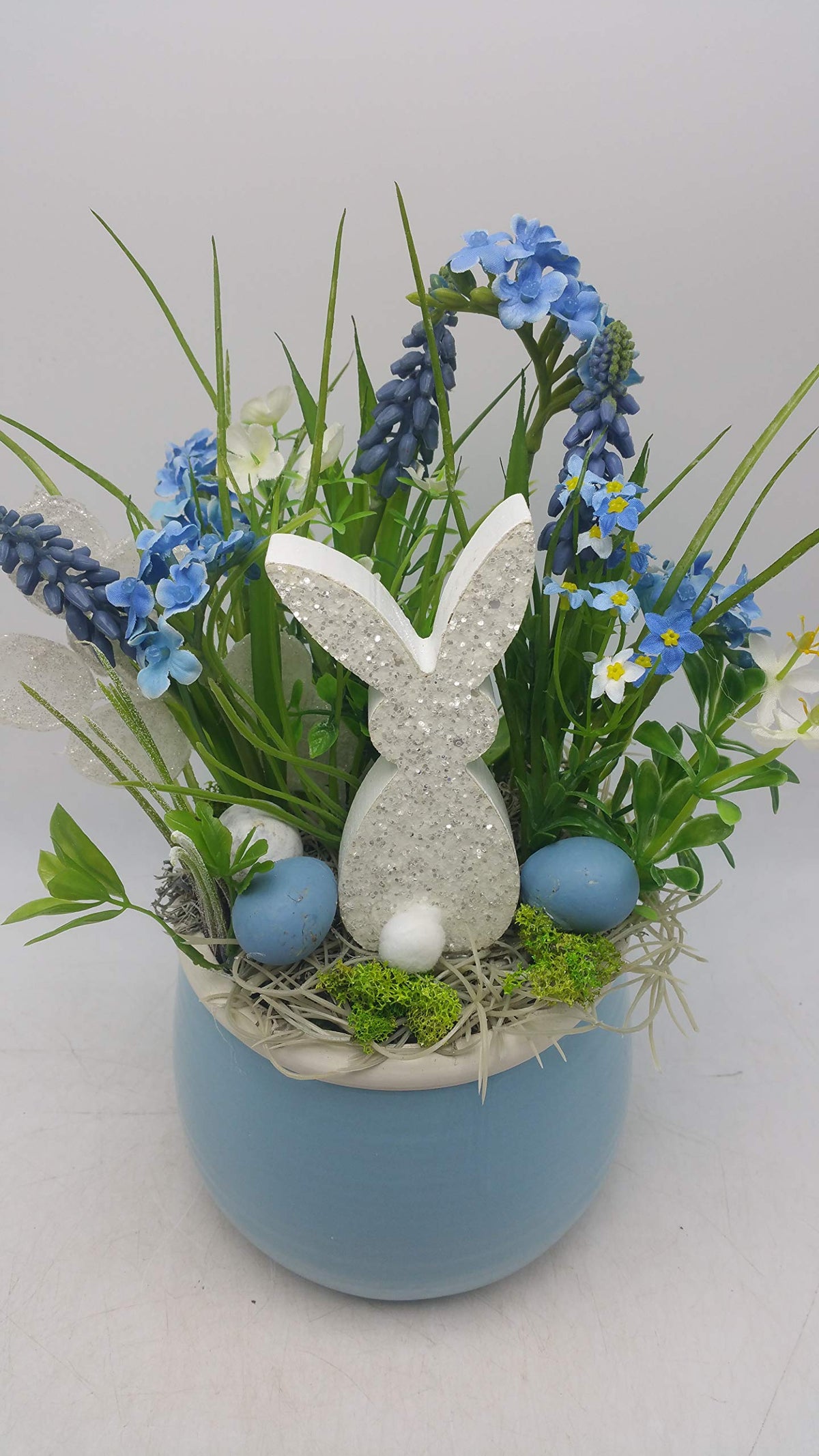 Frühlingsgesteck in Blau und Weiß mit Hase, Vergissmeinnicht, Moos und Stroh im runden Topf, von vorn