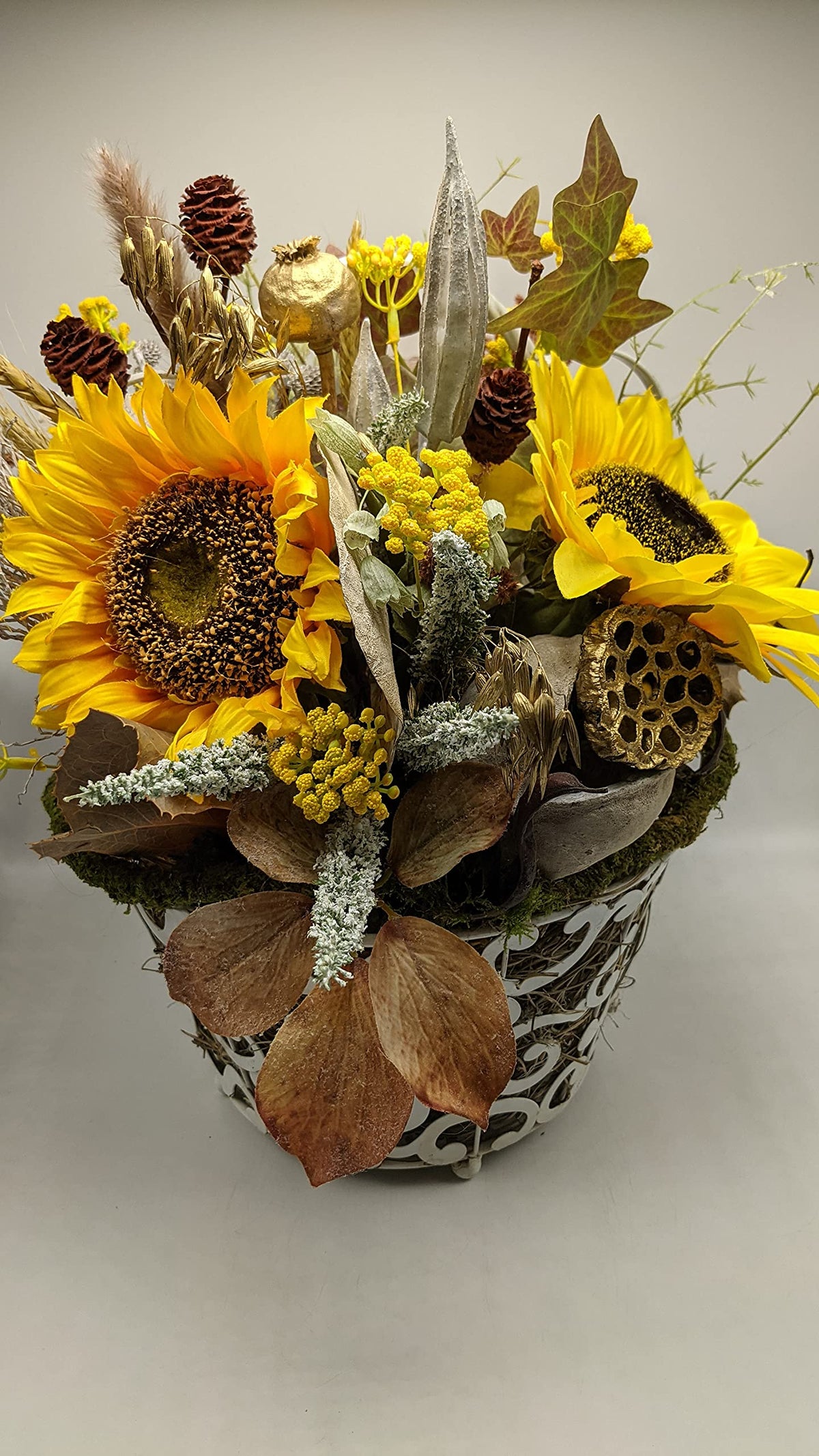 Herbstgesteck mit zwei großen gelben Sonnenblumen, Zapfen, Ähren und Efeu in weißem Metallkorb