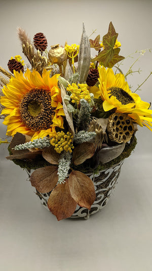 Herbstgesteck mit zwei großen gelben Sonnenblumen, Zapfen, Ähren und Efeu in weißem Metallkorb