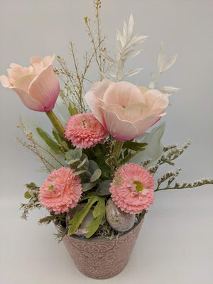 Nahaufnahme des Frühlingsgestecks: geöffnete rosa Anemone, gefüllte Bellis, graugrüne Blätter und helle Trockengräser