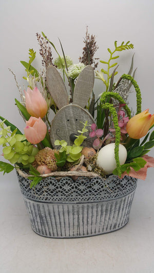Ostergesteck in grauer Zinkschale mit Holzhase, rosa Tulpen, Eukalyptus, weißem Ei und Gräsern