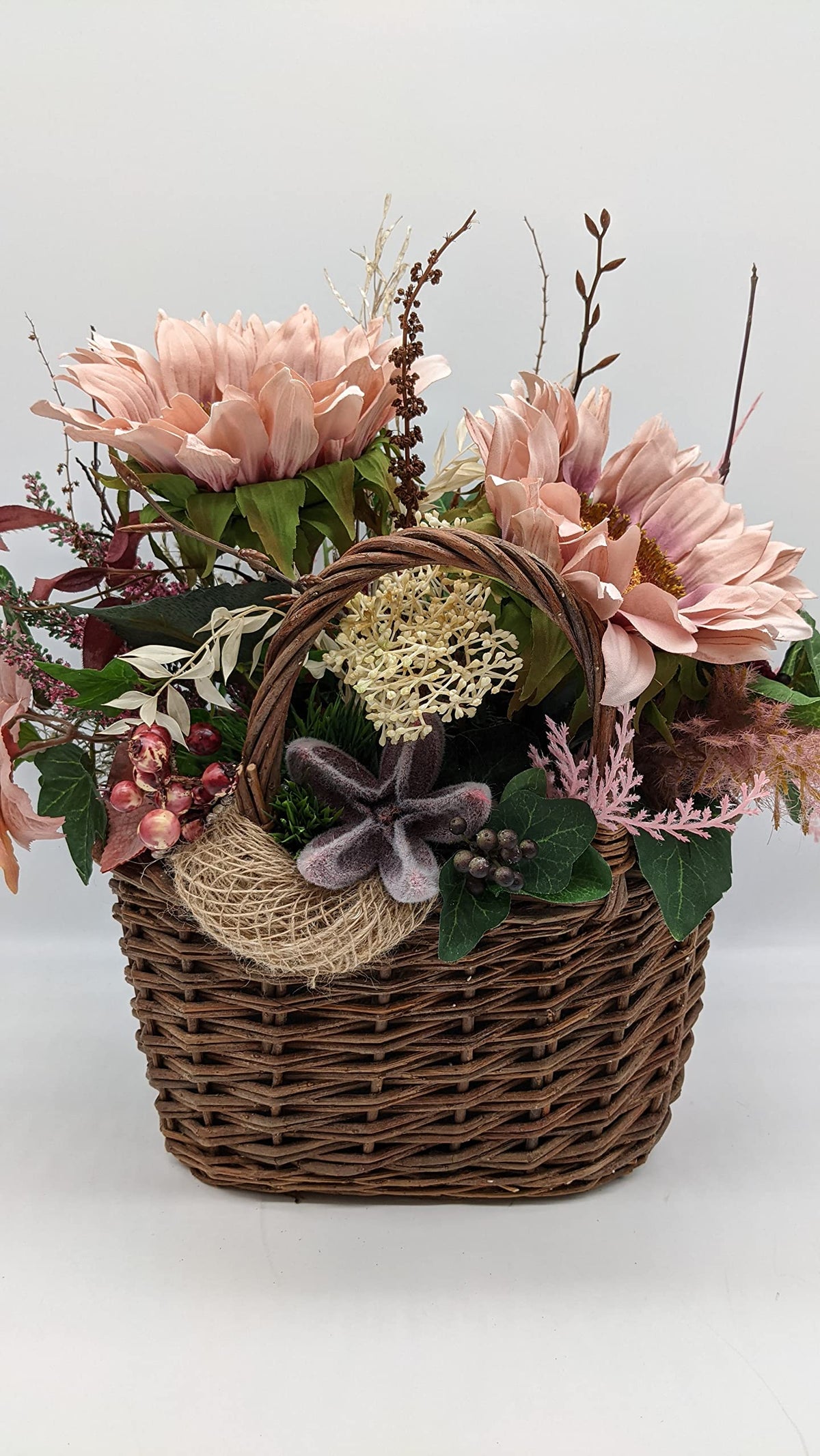 Herbstgesteck im braunen Weidenkorb mit rosa Sonnenblumen, Efeu, Beeren und heller Blütendolde am Henkel