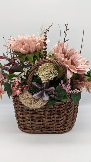 Herbstgesteck im braunen Weidenkorb mit rosa Sonnenblumen, Efeu, Beeren und heller Blütendolde am Henkel