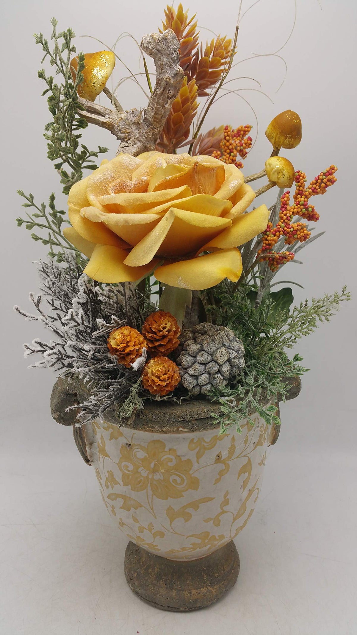 Wintergesteck mit gelber Rose, Glitzerpilzen, Beeren und Zapfen in cremefarbenem Keramiktopf mit gelbem Muster