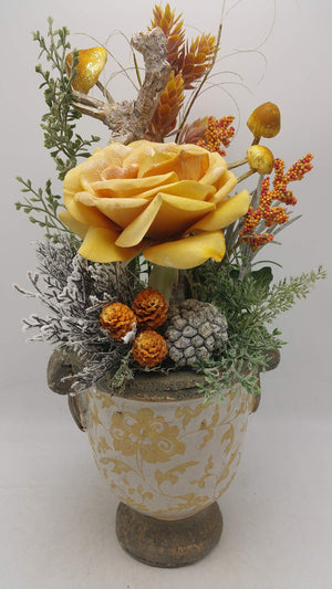 Wintergesteck mit gelber Rose, Glitzerpilzen, Beeren und Zapfen in cremefarbenem Keramiktopf mit gelbem Muster