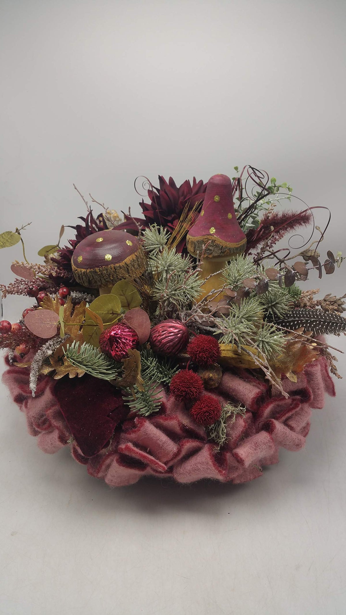 Herbstgesteck in Bordeaux mit zwei Holzpilzen, dunkelroten Chrysanthemen und Tannenzweigen auf rosa Filzkranz