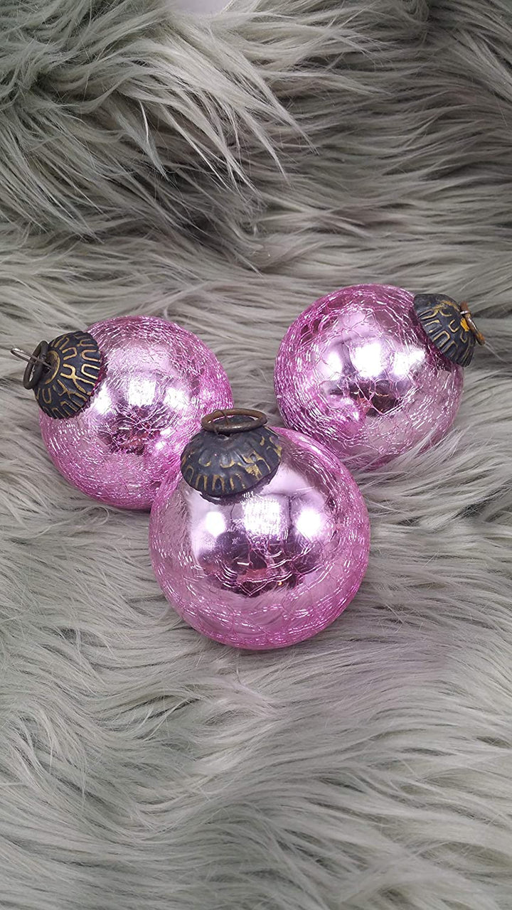 Rosa Bauernglaskugeln mit Craquelé-Oberfläche und dunkler Metallkappe mit Öse auf hellgrauem Fell