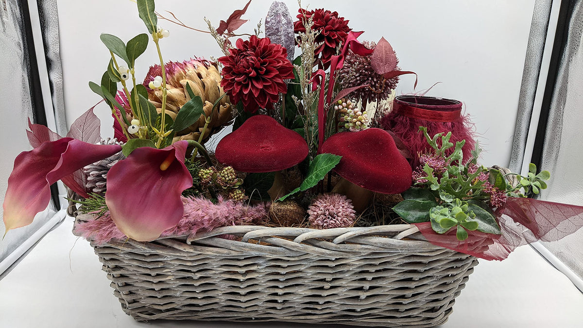 Herbstgesteck im grauen Weidenkorb mit roten Pilzen, bordeauxfarbenen Dahlien, pinken Calla und rotem Teelichtglas